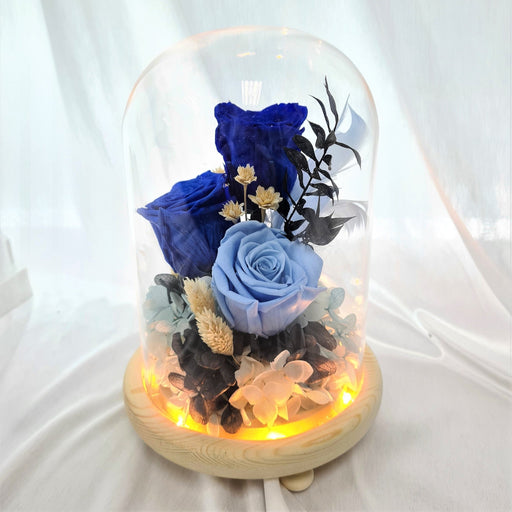 Captivating combination of preserved blue roses, hydrangeas, and dried foliage in glass dome to celebrate the day.