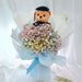 A teddy bear wearing a graduation cap and gown, nestled inside a large bouquet of pastel baby's breath flowers wrapped in white and light blue paper
