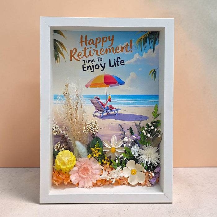Elegant preserved flower frame with soft pastel blooms arranged in a modern white frame, displayed on a minimalist desk beside a workspace, showcasing the product's sophisticated aesthetic and versatile placement options.