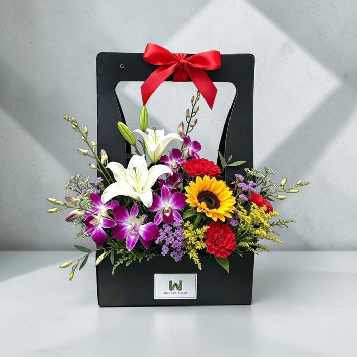 Birthday flower box featuring white lilies, purple orchids, yellow sunflower and red carnations tied with a red bow