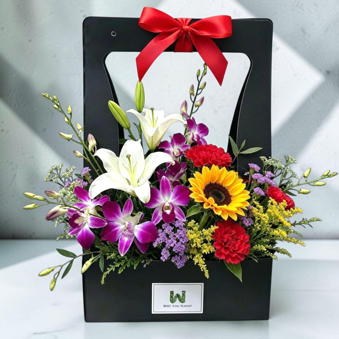 Black gift box arrangement with white lilies, purple dendrobium orchids, sunflower, red carnations and red ribbon bow