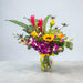 Tropicana Sunrise bouquet in glass vase featuring sunflowers, purple dendrobium orchids and roses