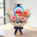 "Turn the Tassel" graduation flower bouquet featuring fresh gerberas, daisies, baby's breath, and a Doraemon graduation bear plush, available for delivery in Singapore.