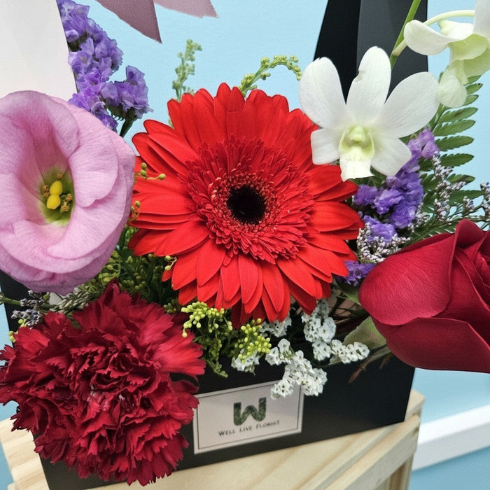 Well Live Florist Bold Delight bloom box with red gerbera, roses, carnations, pink eustoma, and white orchids.