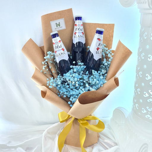 A hand bouquet featuring three bottles of beer placed amidst fresh blue baby's breath flowers, wrapped in brown paper with a yellow ribbon.