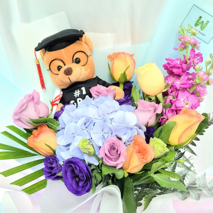Enticing hand bouquet of magnificent roses, eustoma, hydrangea, mathiola and a graduation toy bear