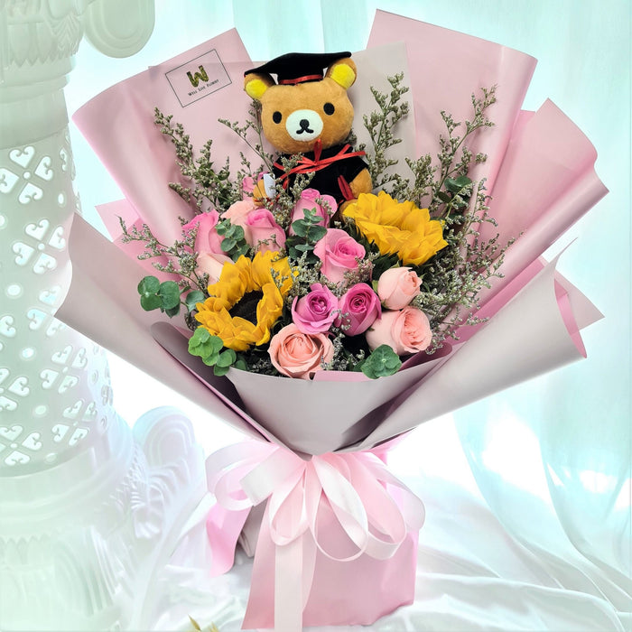 Enticing hand bouquet of magnificent roses, sunflower and a graduation toy bear.