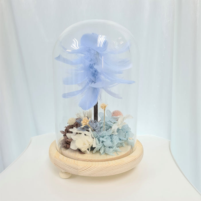 Captivating combination of light blue feather, preserved hydrangeas and dried foliage in glass dome to celebrate the day