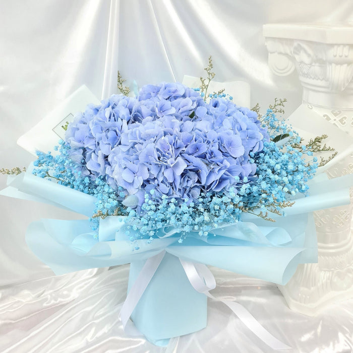 Mesmerising hand bouquet of dazzling blue hydrangea, baby's breath, and foliage.