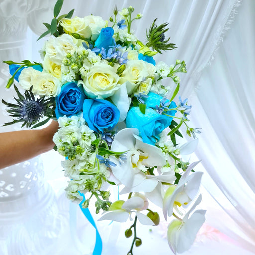 Exquisite hand bouquet of enticing blue roses, eustoma, Phalaenopsis orchid, mathiola and foliage.